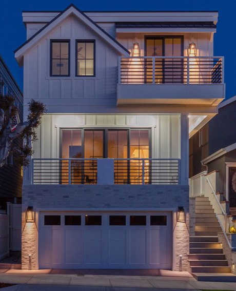 Three story modern farmhouse exterior lit at dusk